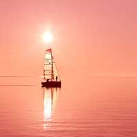 Boat sailing under the red sun on a lake
