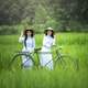 two-asian-girls-riding-a-bicycle-through-a-field